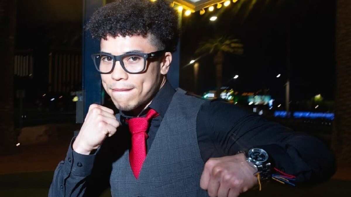 Abel Mendoza posing at night wearing glasses, vest, and red tie