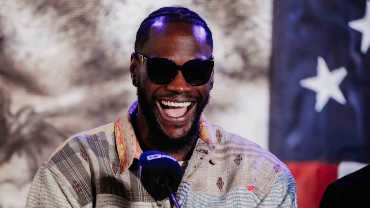 Deontay Wilder smiles during a media appearance with a United States flag behind him