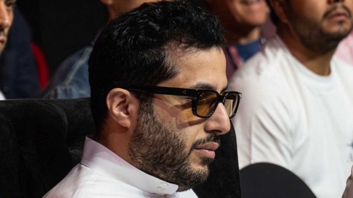 Turki Alalshikh wearing glasses and traditional Saudi clothing while seated at a boxing event, viewed in profile