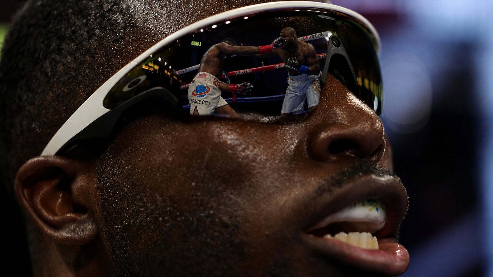 Close-up of Joshua Edwards wearing reflective sunglasses with a boxing action scene visible in the lens reflection
