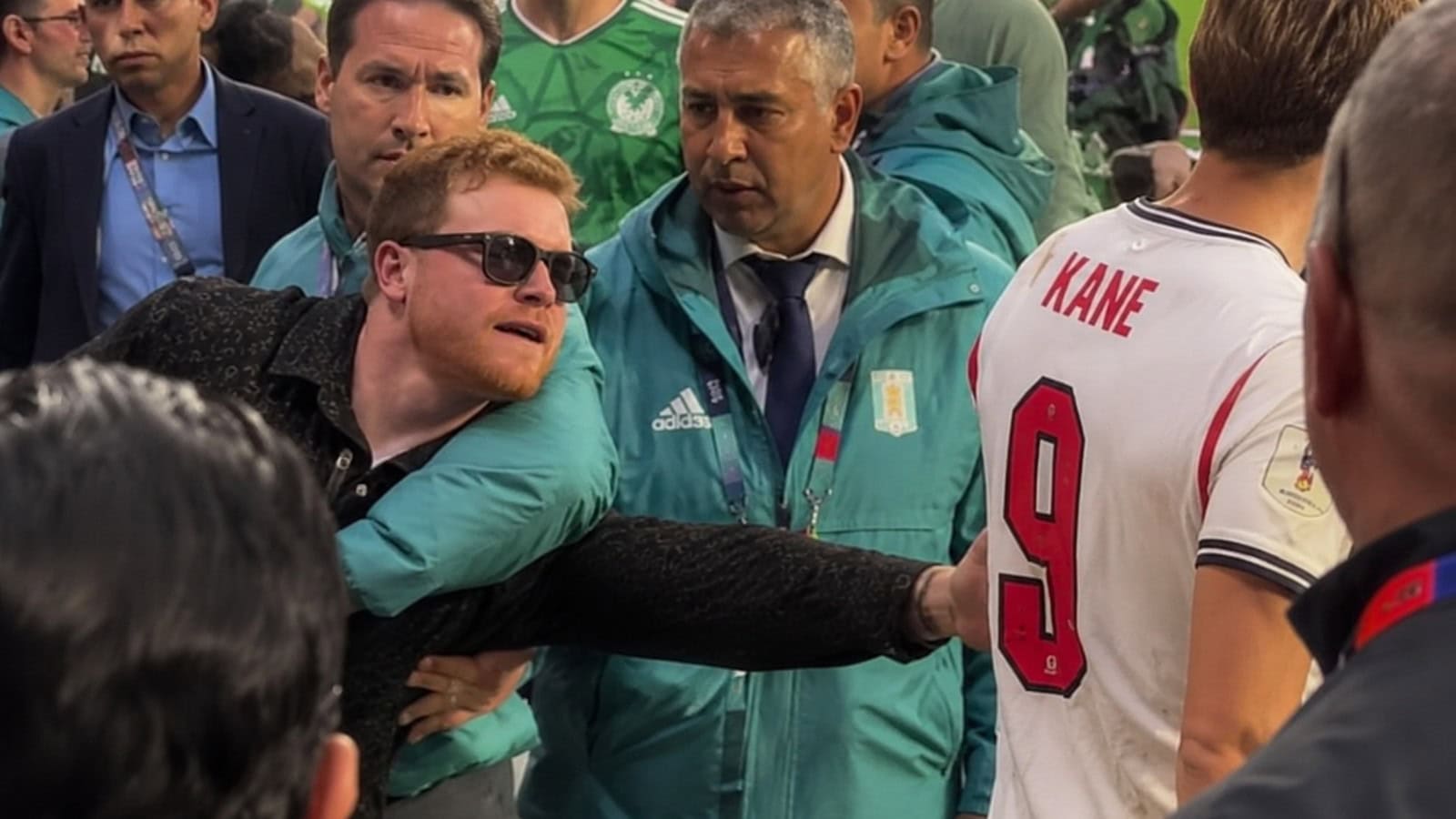 Canelo Alvarez is held back by World Cup security as he reaches toward Harry Kane at Mexico vs England