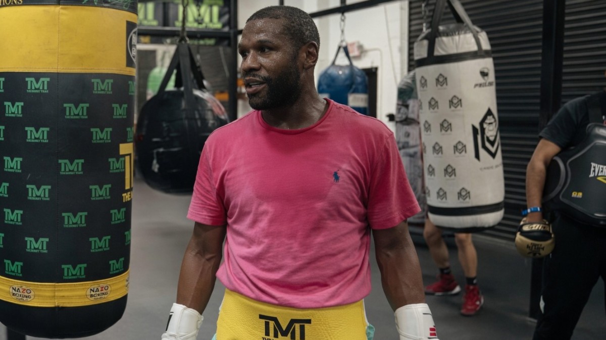 Floyd Mayweather stands inside his boxing gym wearing a pink T-shirt and yellow TMT body protector during a training session