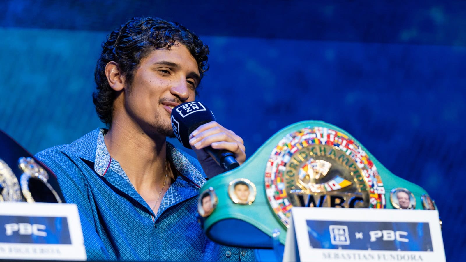 Sebastian Fundora speaks into a DAZN microphone with his WBC super welterweight title belt at a PBC press conference