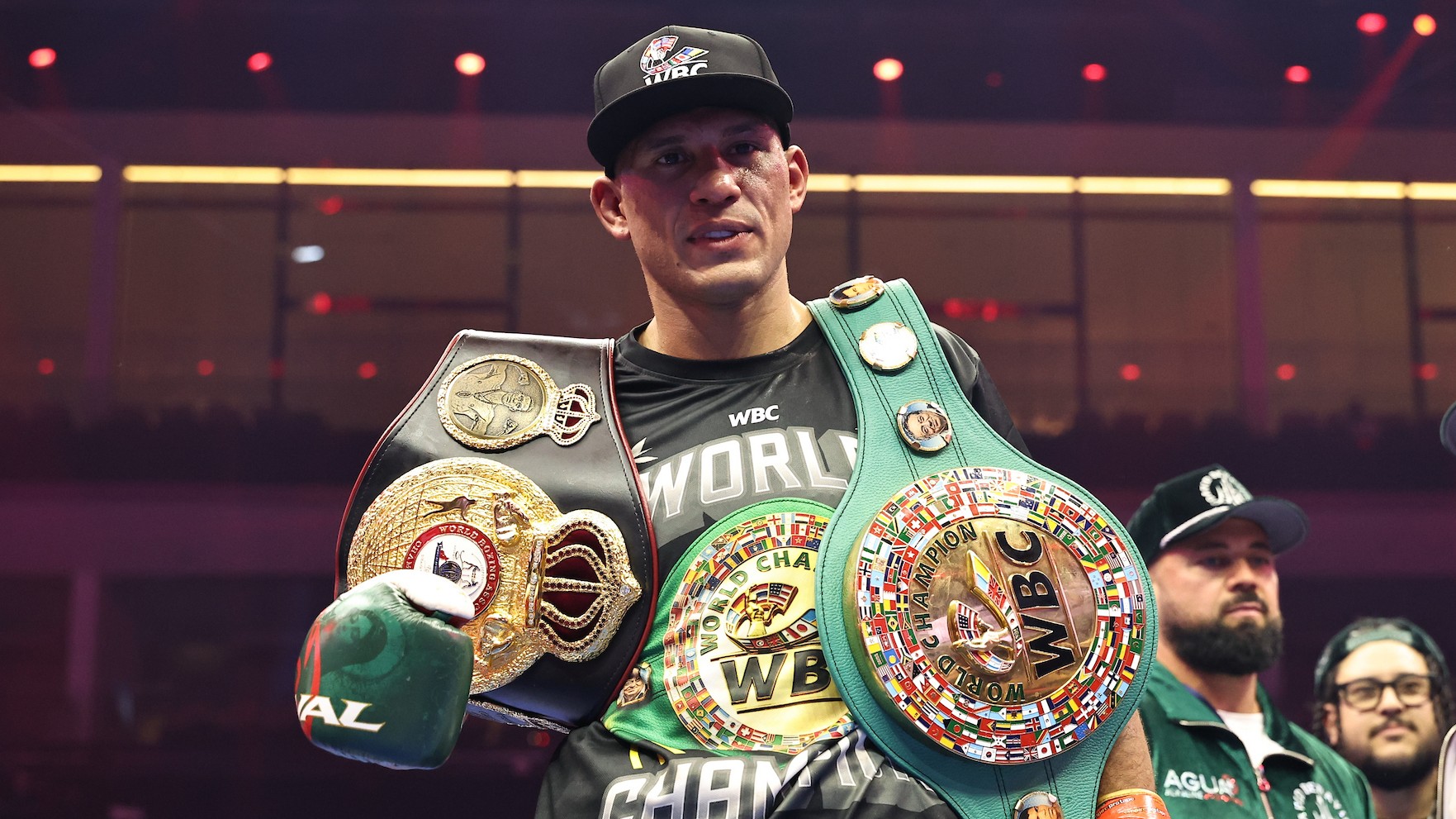 David Benavidez wearing WBC championship belts and a black cap following a boxing victory