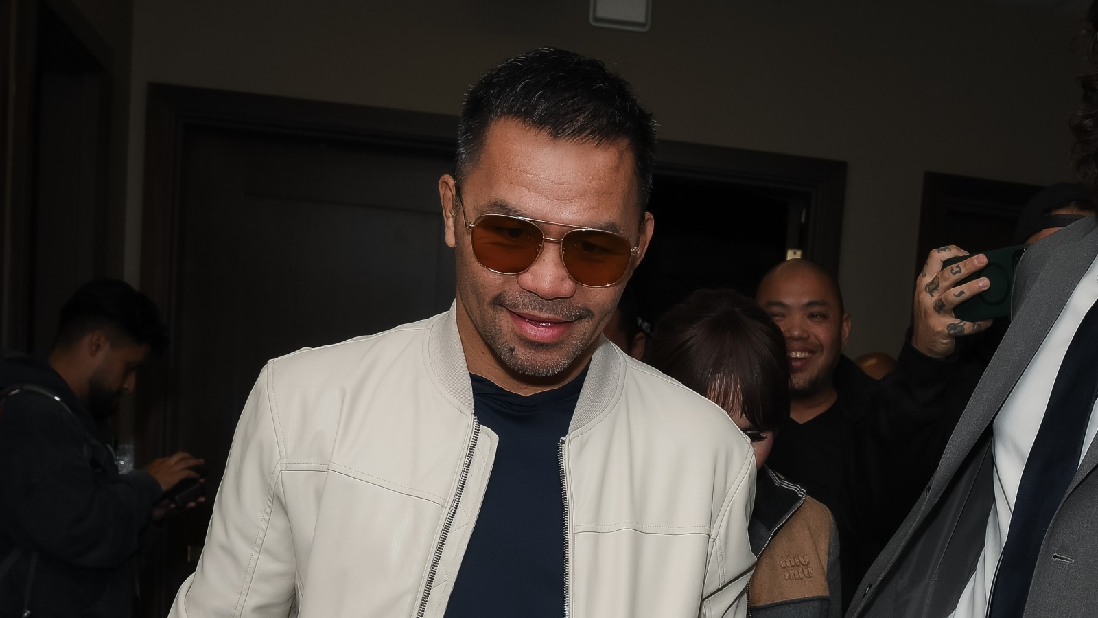 Manny Pacquiao wearing sunglasses and a white jacket while attending an event surrounded by fans and members of his entourage