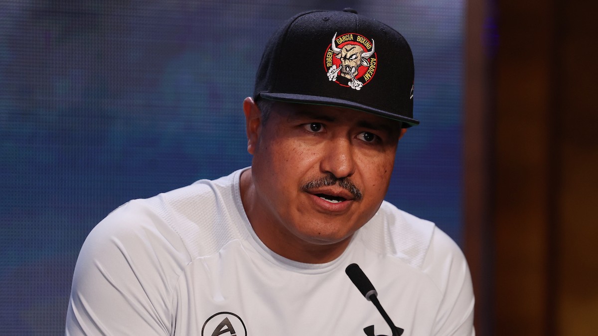 Robert Garcia speaking into a microphone while wearing a Robert Garcia Boxing Academy cap at a boxing press conference